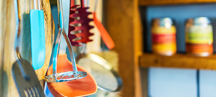 Utensils hanging in a kitchen near a shelf with jars on it