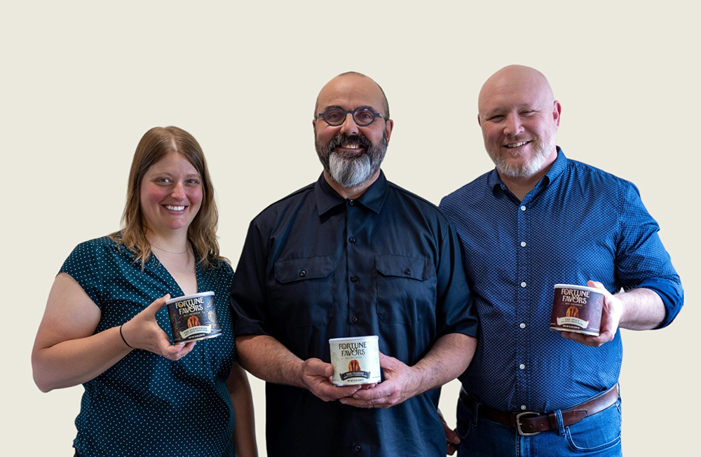 Three people holding Fortune Favors cans of nuts