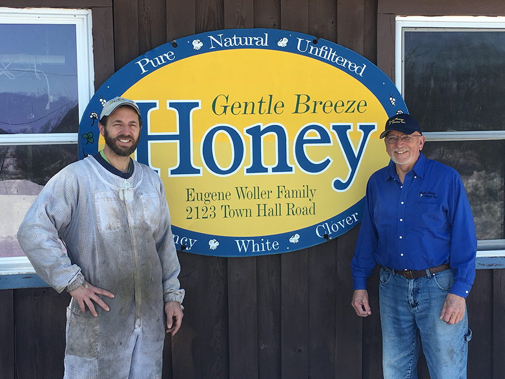 Two people standing on either side of the Gentle Breeze Honey sign on the side of a building