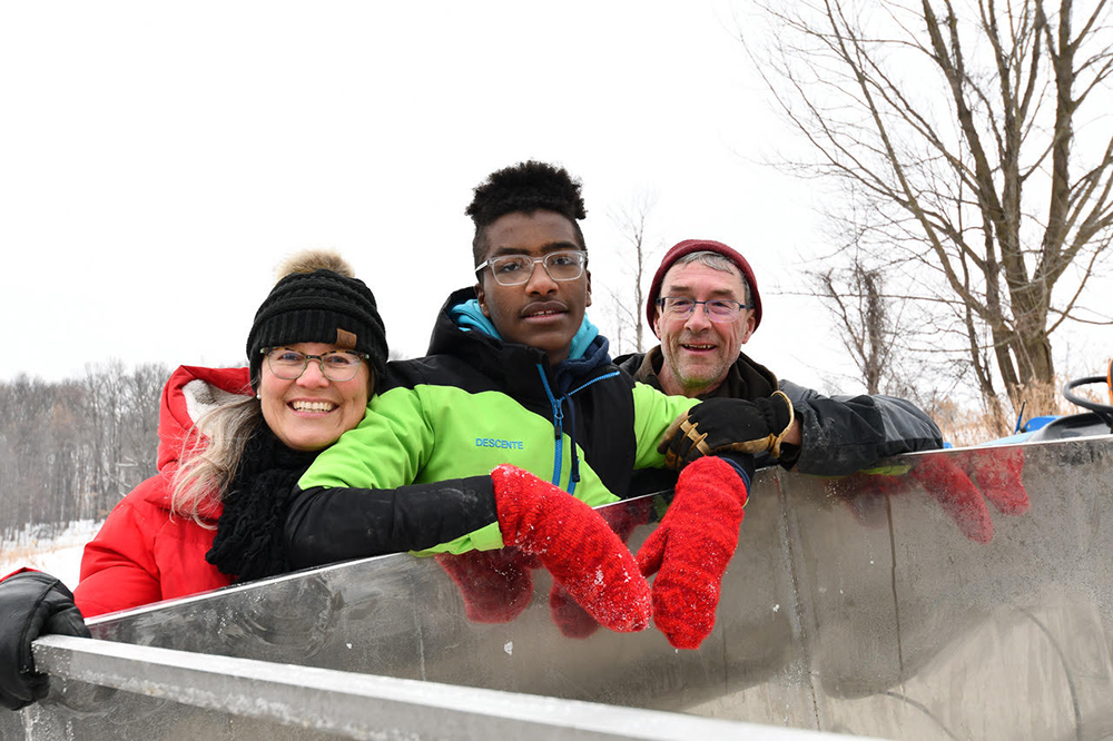 Three people leaning over the edge of a large bin and dressed up in winter gear