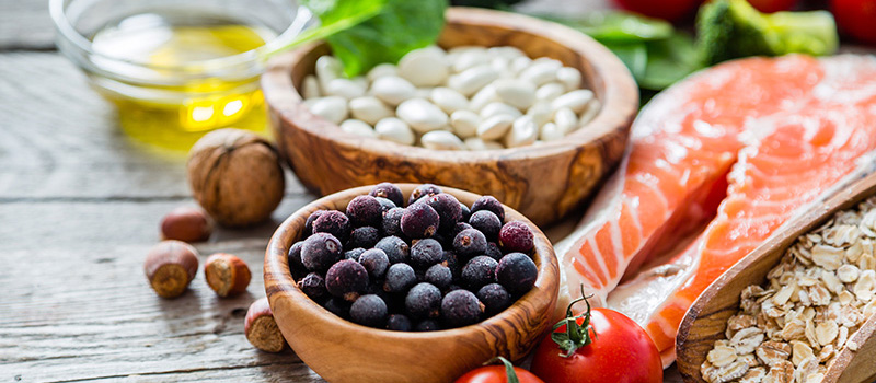 A table with olive oil, beans, blueberries, fish, nuts, oats and tomatoes spread on it