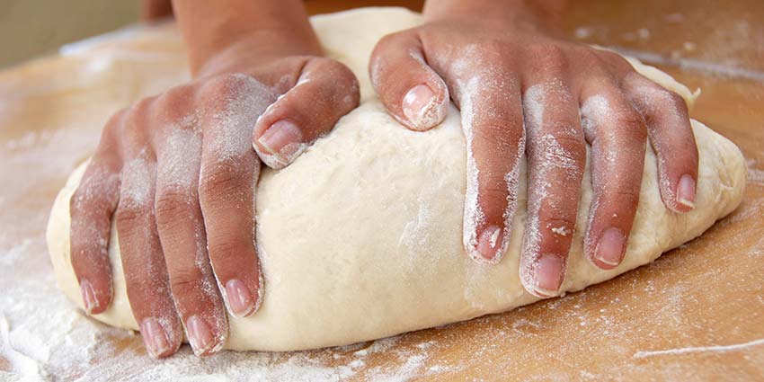 A person kneading dough on a wooden surface