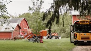 A school bus parked outside a farm, with barn and equipment