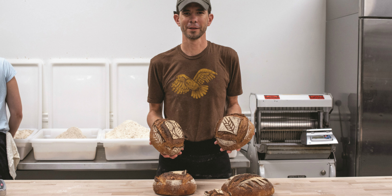 A man holding up two loaves of bread in an industrial kitchen