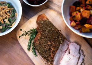 Herb encrusted turkey breast sliced on a cutting board surrounded by bowls of side dishes