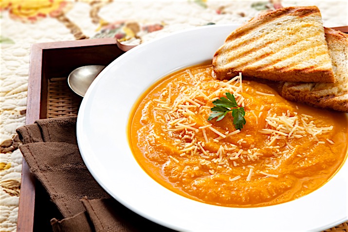 Pumpkin soup with parmesan cheese and crusty toasted bread, on a serving tray.