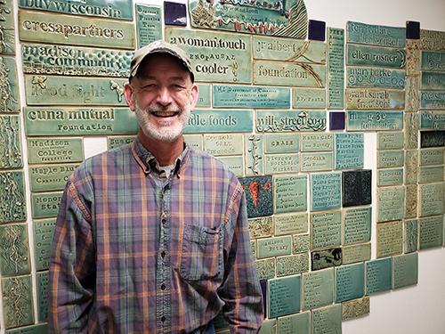 Chris Brockel standing in front of a wall that has tiles with names on it