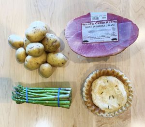 Potatoes, a small ham, asparagus, and a pie on a table, top view