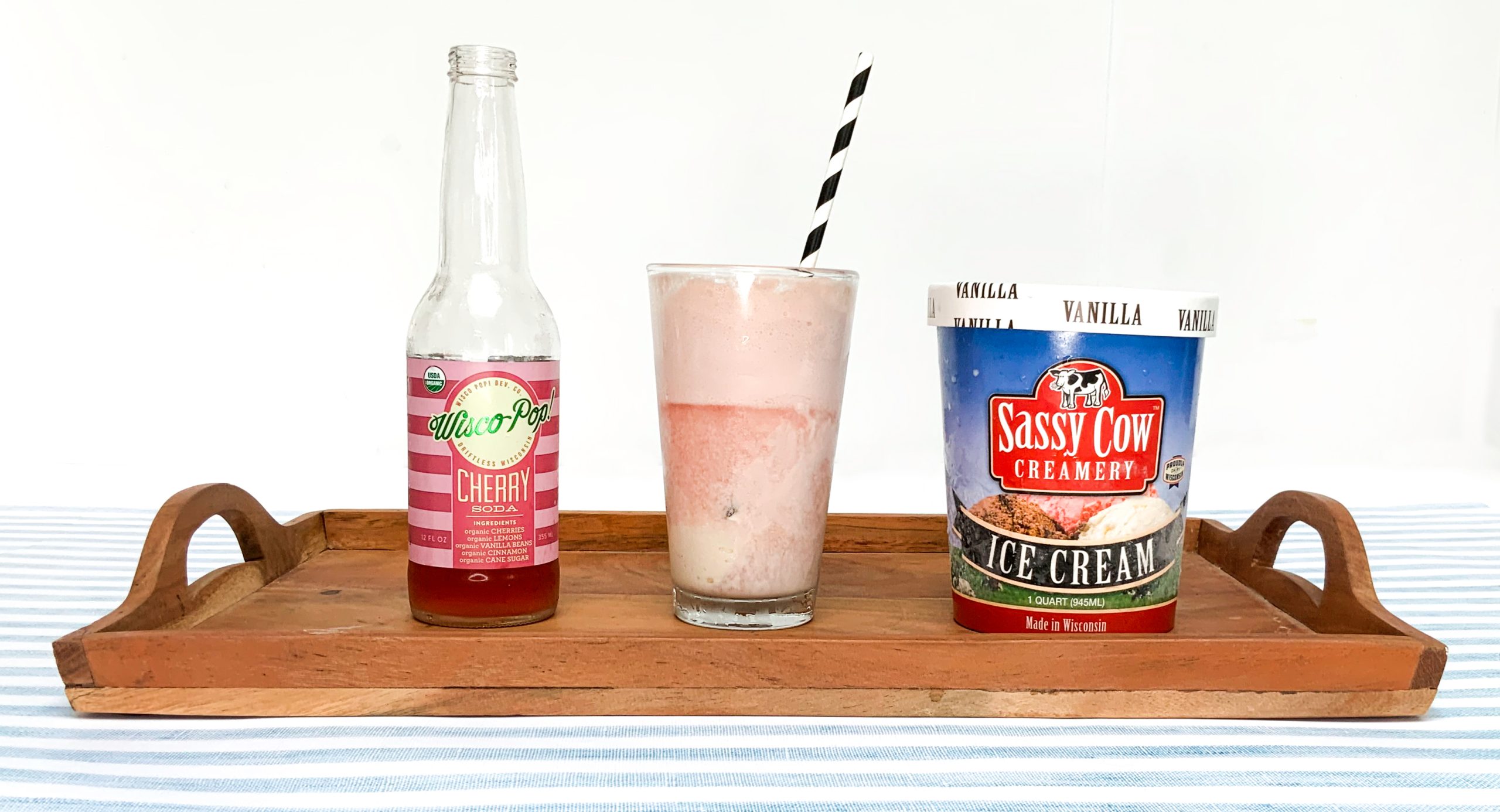 A bottle of Wisco-Pop cherry soda, a half eaten ice cream float, and a pint of Sassy Cow vanilla ice cream lined up on a tray