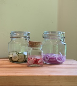 three jars of pickled vegetables. From left: cucumbers, radishes, red onions