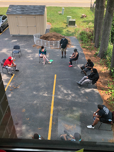 A group of teens sitting in chairs in a circle in a parking lot