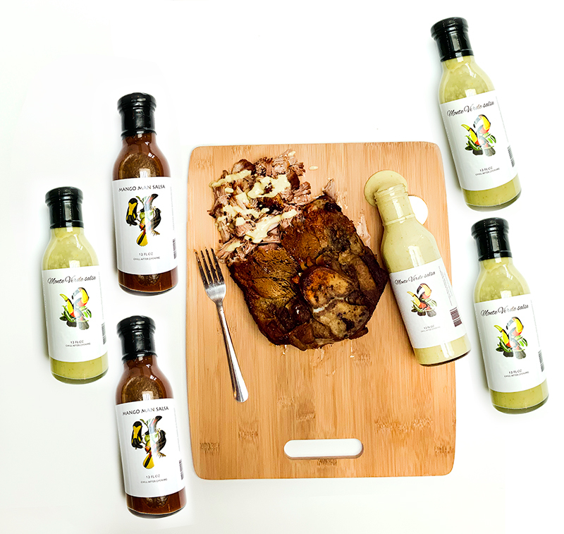 A hunk of meat on a cutting board surrounded by six bottles of different sauces