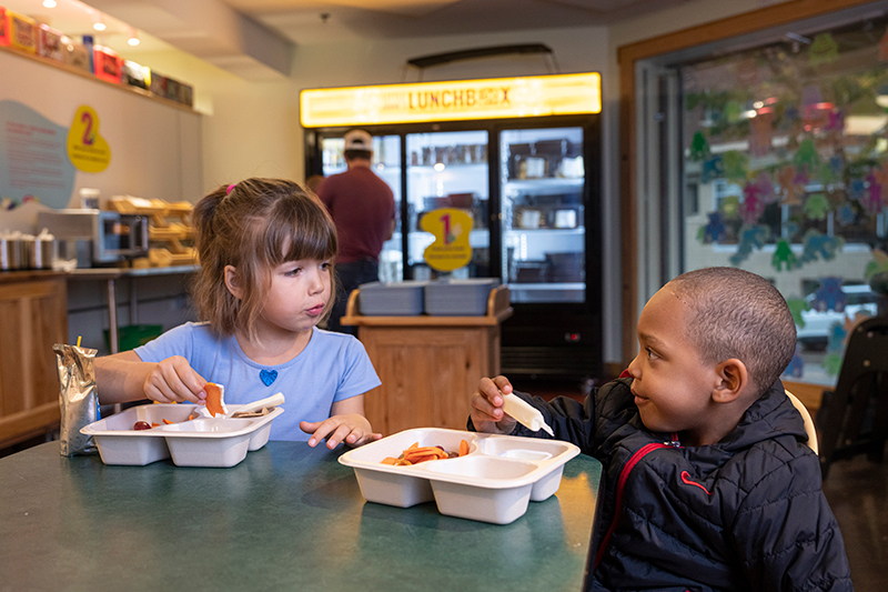 Two children sitting at a table eating out of takeout containers