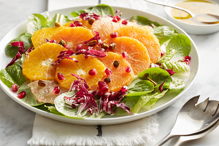 A salad on a plate with slices of orange cross sections on top