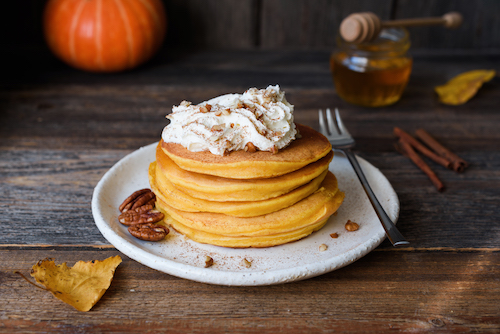 Pumpkin pancakes with whipped cream and cinnamon on old wooden table. Autumn comfort food, breakfast