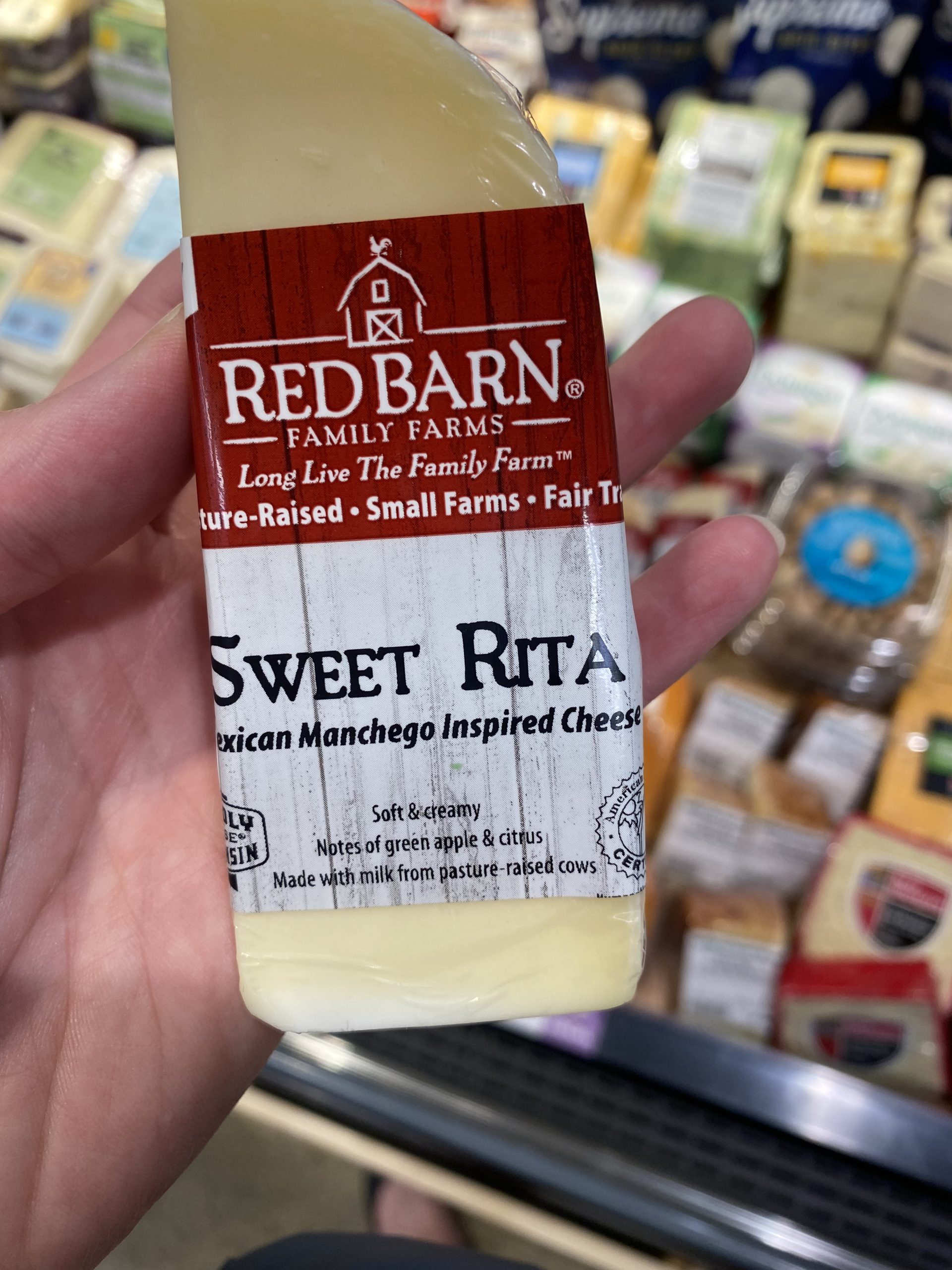 A person holding a wedge of Red Barn sweet rita manchego cheese