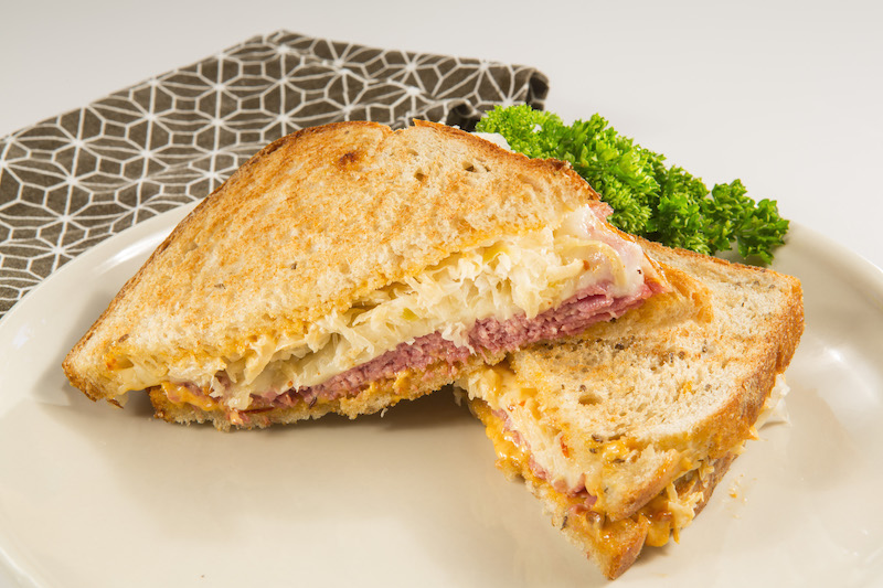 A reuben sandwich on a plate with parsley and a napkin next to it