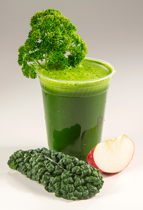 A green smoothie with a sprig of parsley, a kale leaf, and an apple slice around it