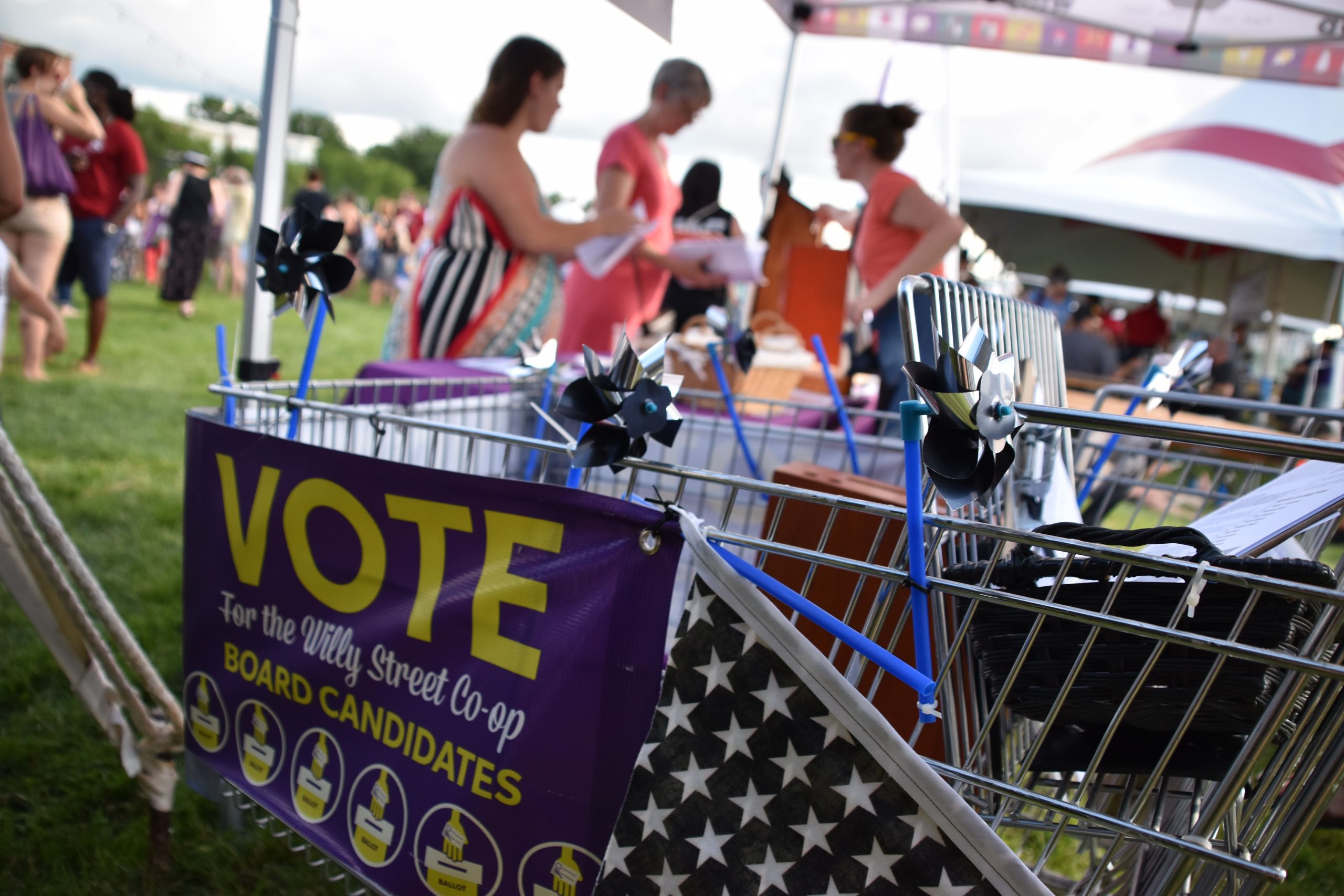 A sign promoting voting for the Willy Street Co-op board attached to a shopping cart at an outdoor festival