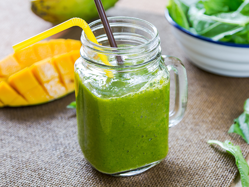 A sliced mango next to a green smoothie in a jar with a straw