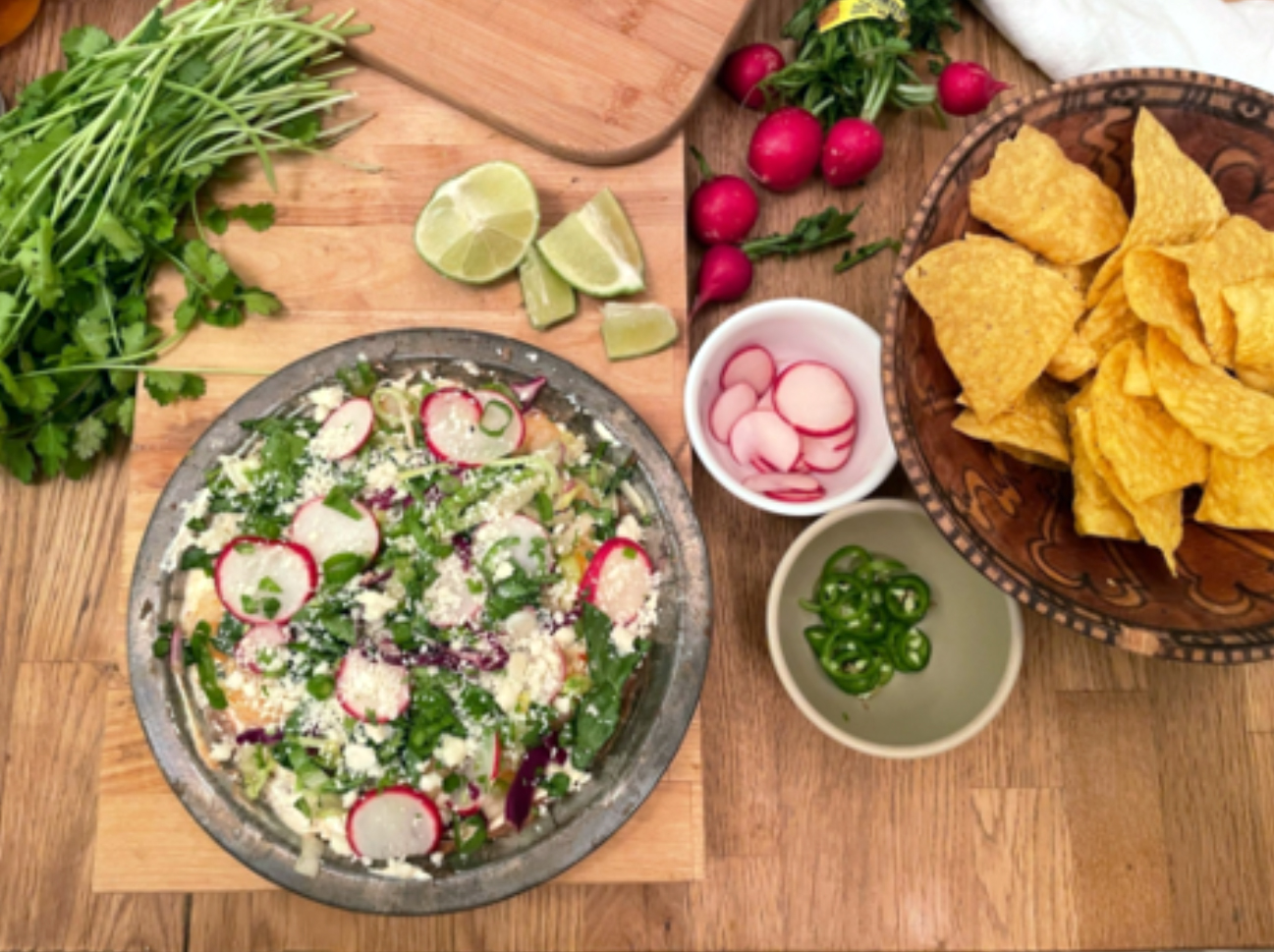 A cutting board with bowls of dips and chips and chopped limes and cilantro on it