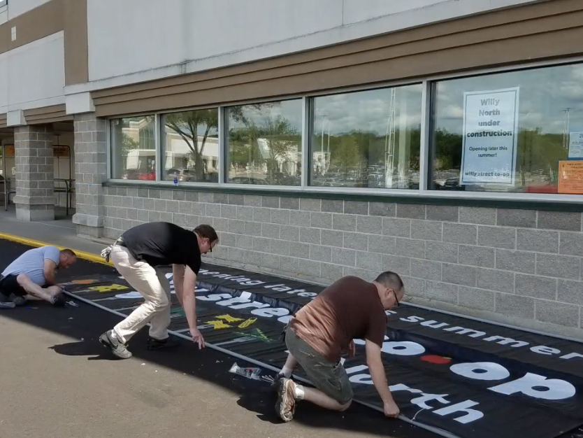 Three men prepping a sign to be hung outside Willy Street Co-op North